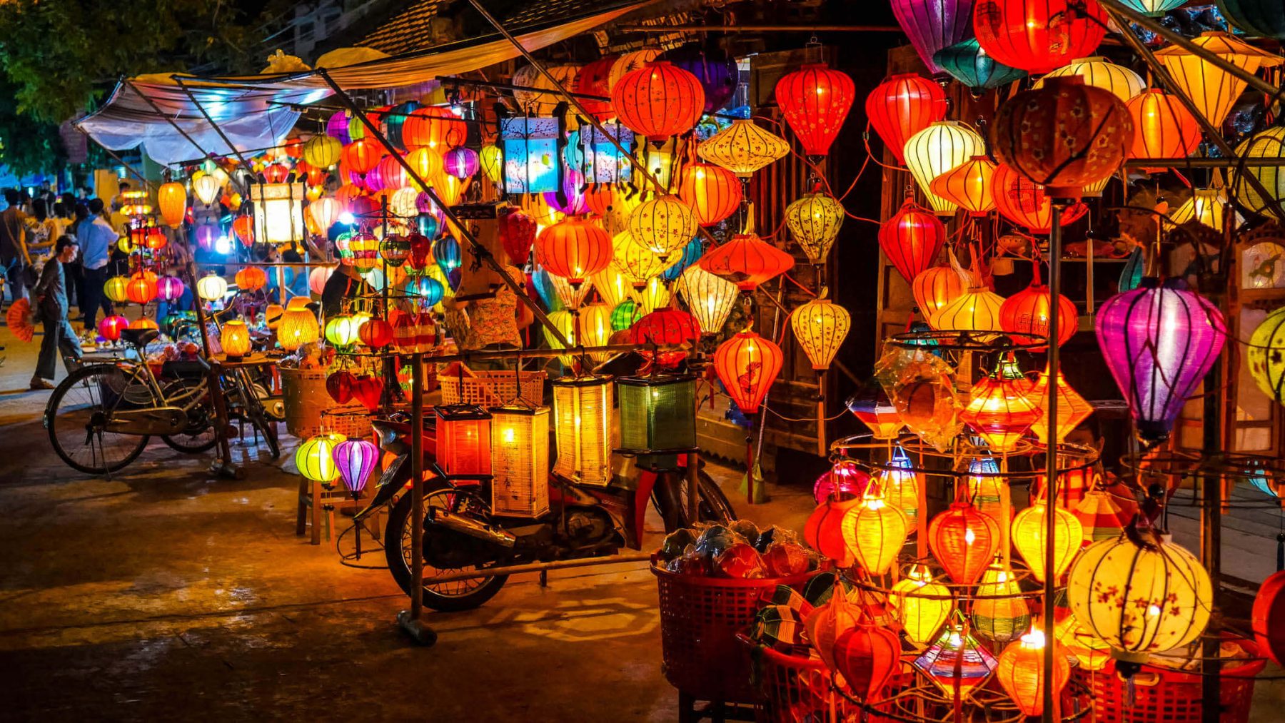 Chợ đêm Hội An sôi động với các quầy bán đèn lồng, đồ thủ công và nhiều loại thức ăn đường phố khác nhau, nhộn nhịp người qua lại.